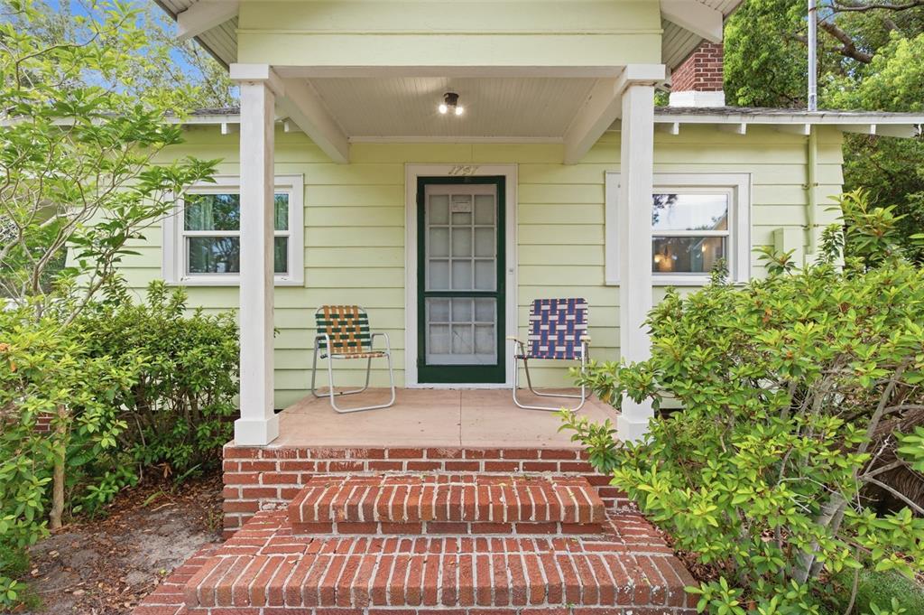 A light green house with a brick porch, two chairs, and a white front door — 1747 APACHE TRAIL, CLEARWATER, FL