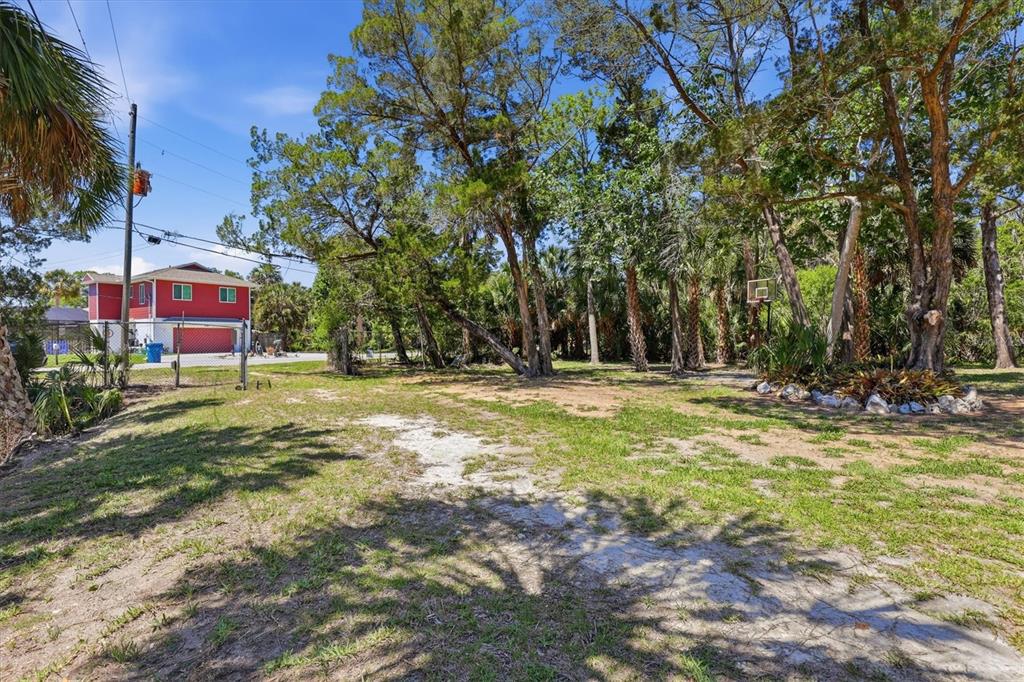A grassy yard with scattered trees and a basketball hoop near a red house — 6240 COLONY CIRCLE, WEEKI WACHEE, FL