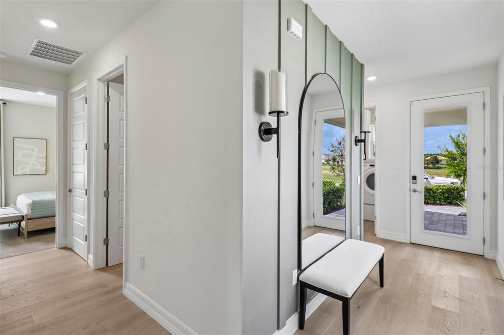 A bright entryway features light wood floors, a sage green accent wall, and a bench — 3945 KENNEBUNK LOOP, MOUNT DORA, FL