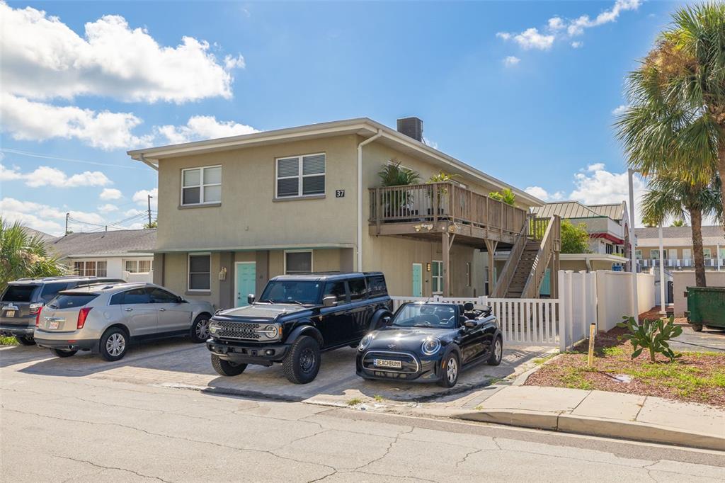 A two-story tan building with a wooden deck, outdoor staircase, and three parked cars — 37 144TH AVENUE, MADEIRA BEACH, FL