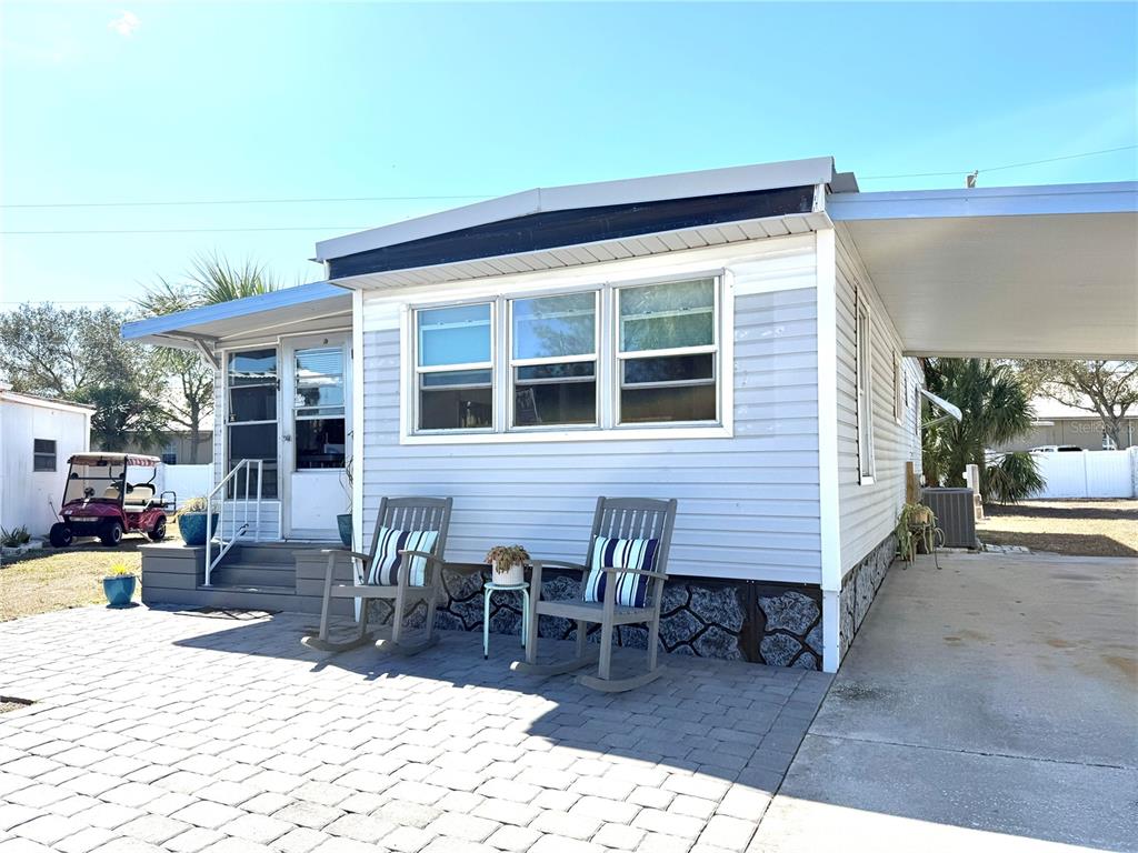 A light blue mobile home features a paved patio, two rocking chairs, and a carport — 308 S PORT ROYAL LANE, APOLLO BEACH, FL
