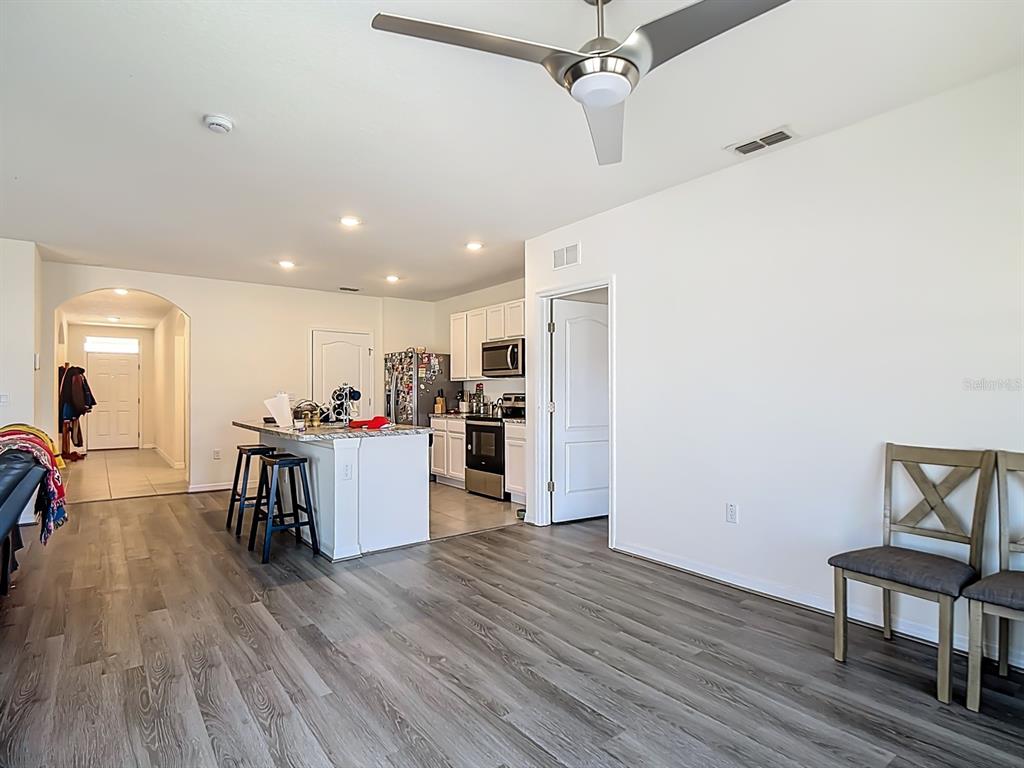 An open-concept kitchen and living area features wood-look flooring, white cabinetry, and a ceiling fan — 132 SOFIA LANE, LAKE ALFRED, FL