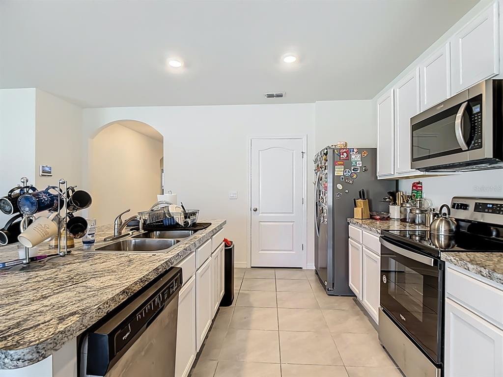 A kitchen features white cabinets, granite countertops, stainless steel appliances, and tile flooring — 132 SOFIA LANE, LAKE ALFRED, FL