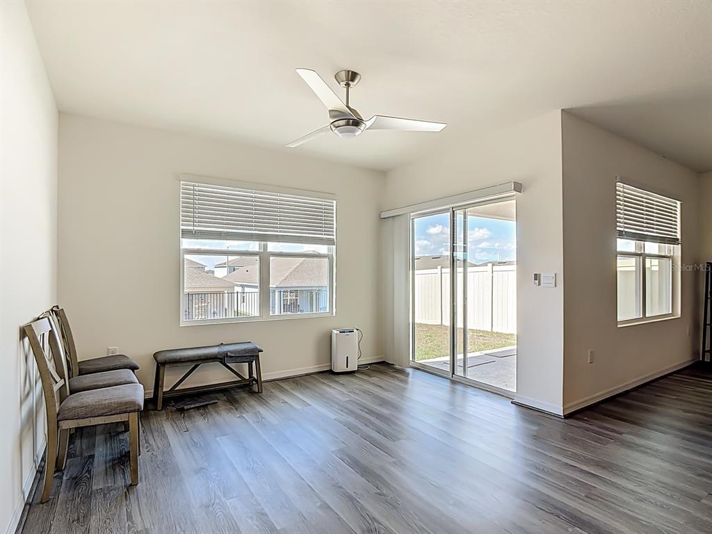 A living room with wood-look flooring, a ceiling fan, large windows, and a sliding glass door — 132 SOFIA LANE, LAKE ALFRED, FL