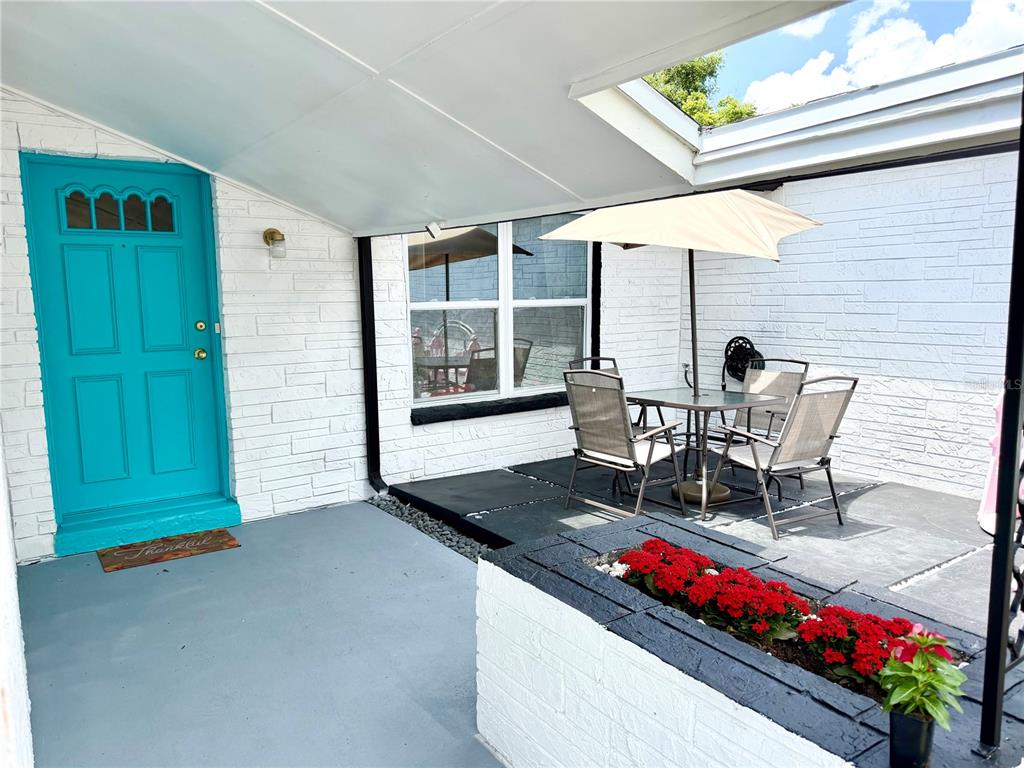 A patio area features a bright blue door, a dining set with an umbrella, and planters — 143 VALLEY CIRCLE, BRANDON, FL