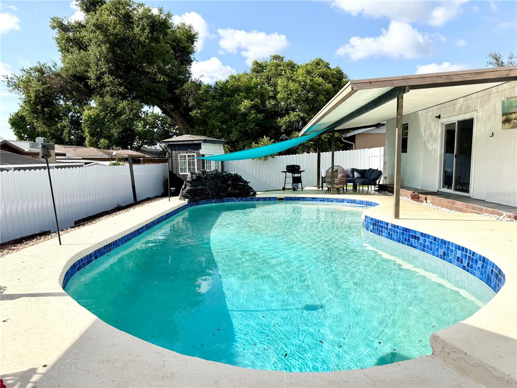A backyard features a swimming pool with blue tile trim, a patio, and a shade sail — 143 VALLEY CIRCLE, BRANDON, FL
