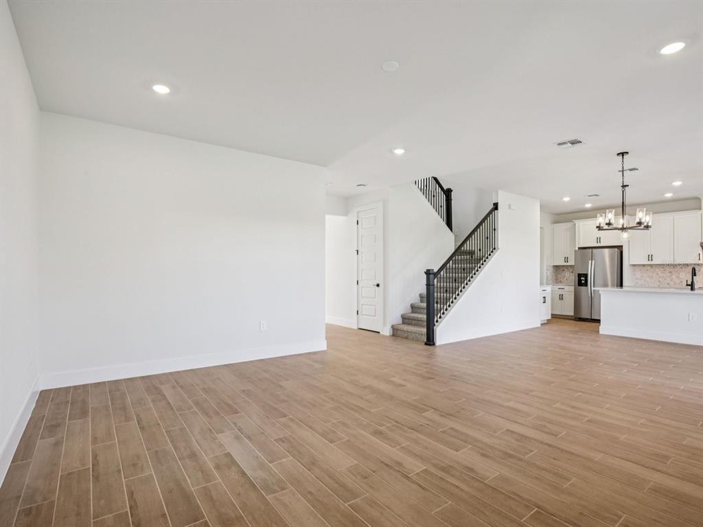 A bright, open-concept living area features wood-look tile flooring, a staircase, and a kitchen — 156 SHADY EDGE LOOP, NOKOMIS, FL