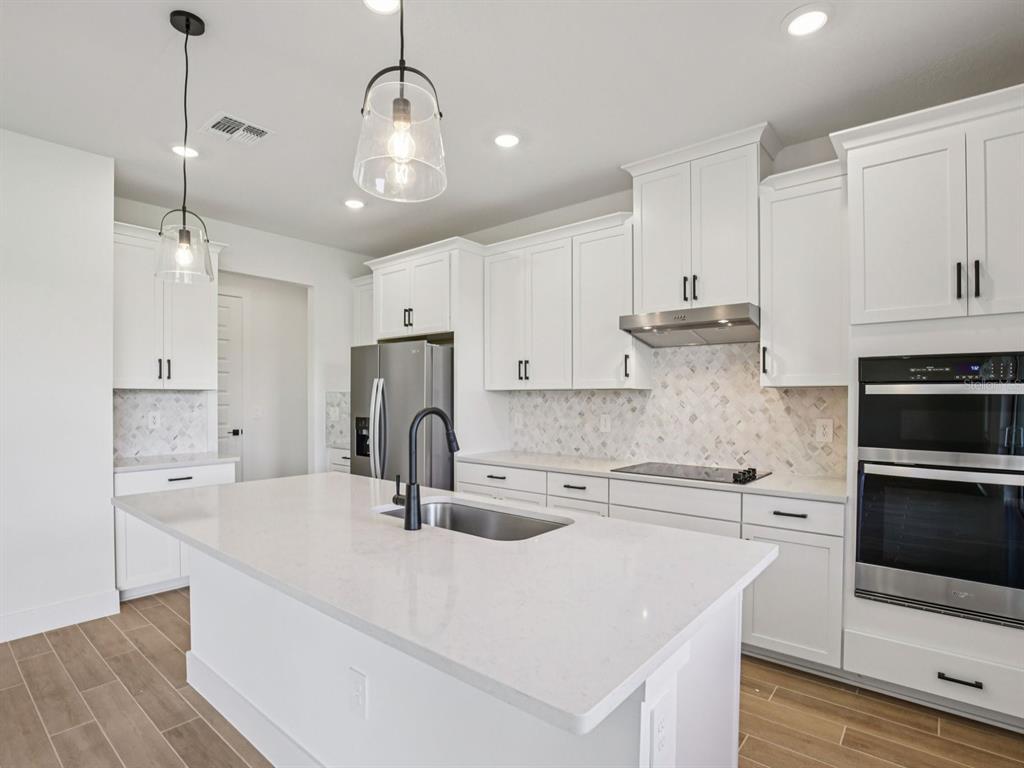 A modern kitchen features white cabinetry, a large quartz island, and stainless steel appliances — 156 SHADY EDGE LOOP, NOKOMIS, FL