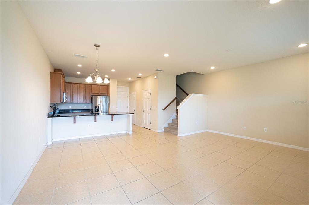 An open-concept kitchen with wood cabinets and a breakfast bar overlooks a tiled living area — 2617 GIARDINO LOOP, KISSIMMEE, FL