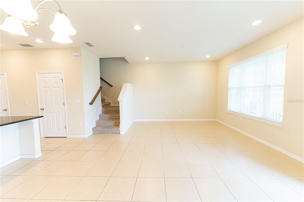 An open-concept room features light-colored tile flooring, a staircase, and a large window — 2617 GIARDINO LOOP, KISSIMMEE, FL