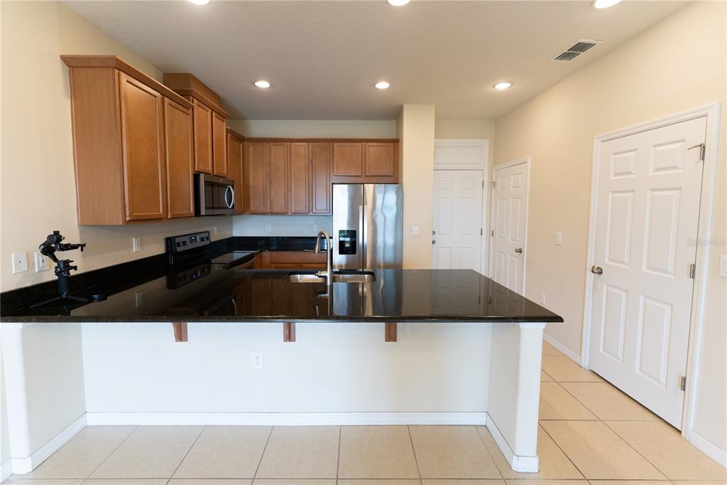 A kitchen features wood cabinets, black countertops, stainless steel appliances, and tile flooring — 2617 GIARDINO LOOP, KISSIMMEE, FL