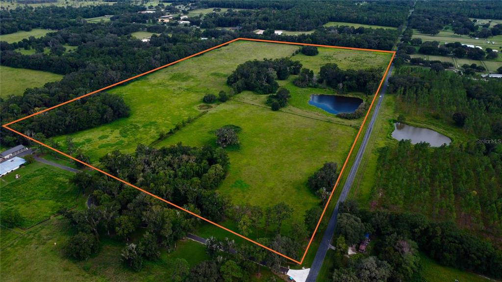 An aerial view shows a large, fenced grassy pasture with trees and a small pond — NW 110TH AVENUE, REDDICK, FL
