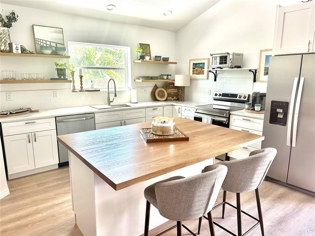 A bright kitchen features white cabinetry, a wood-topped island, and open shelving — 7233 MIDNIGHT PASS ROAD, SARASOTA, FL