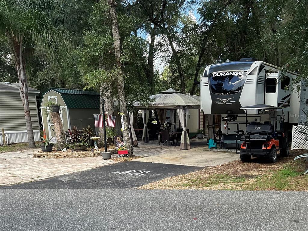 A fifth-wheel RV, a gazebo, and a storage shed sit on a paved lot — 25191 NE 142ND PLACE, FORT MC COY, FL