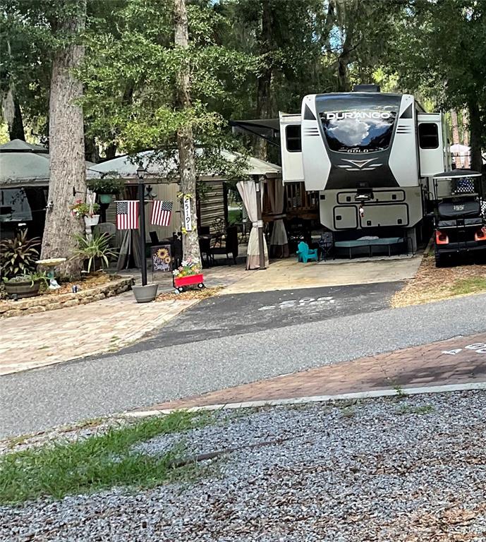 A large fifth-wheel camper is parked on a paved lot next to a covered patio — 25191 NE 142ND PLACE, FORT MC COY, FL