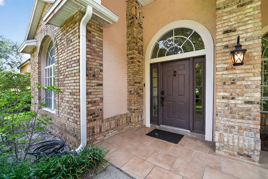 A brick-front home entrance features a brown door, arched transom window, and tiled porch floor — 7691 BELVOIR DRIVE, ORLANDO, FL