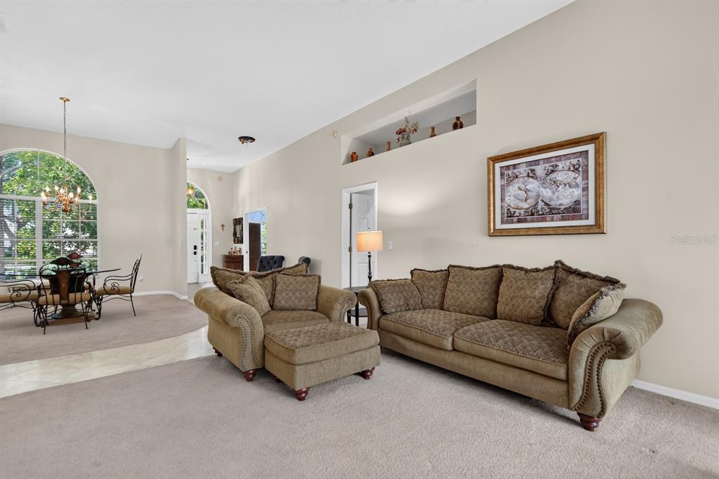 A living room with beige carpet, a sofa, an armchair with ottoman, and a dining area — 7691 BELVOIR DRIVE, ORLANDO, FL