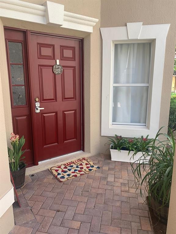 A red front door with a sidelight and a brick patio entrance with potted plants — 6956 BRESCIA WAY, ORLANDO, FL