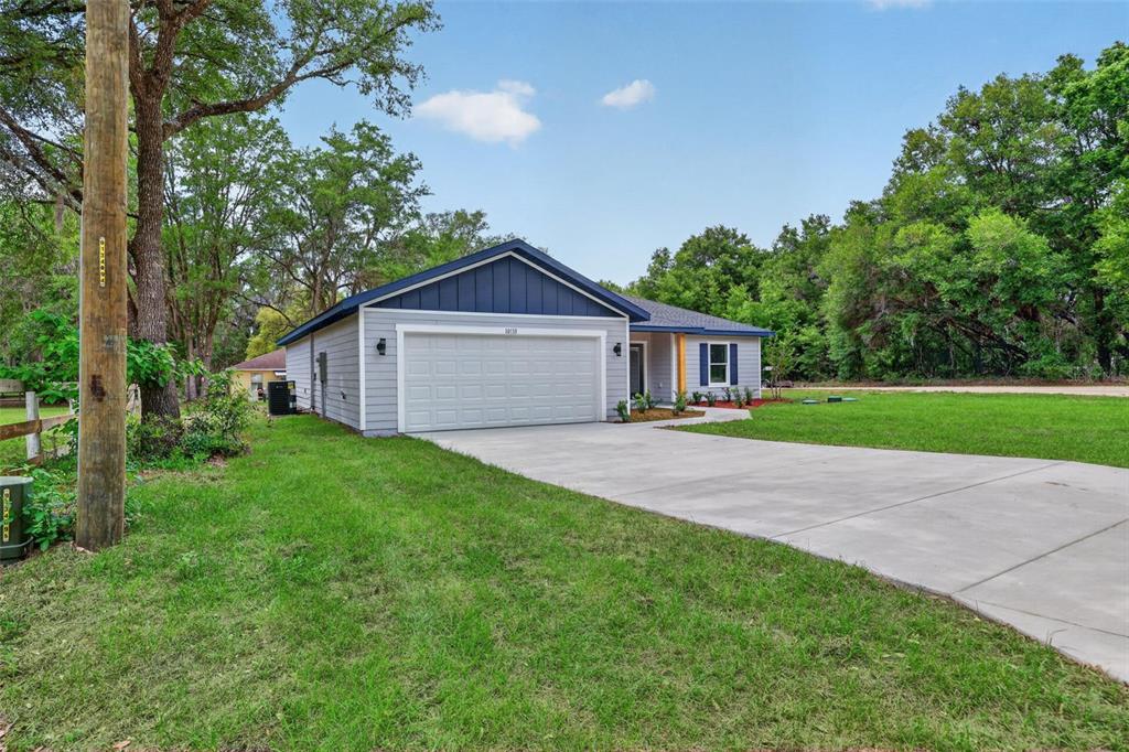 A single-story house with light gray siding, a blue gable roof, and a concrete driveway — 13932 SW 104TH LANE, DUNNELLON, FL