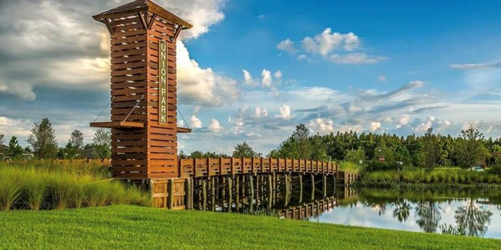 A wooden tower and bridge stand over a pond in a grassy park setting — 32971 PEZ LANDING LANE, WESLEY CHAPEL, FL