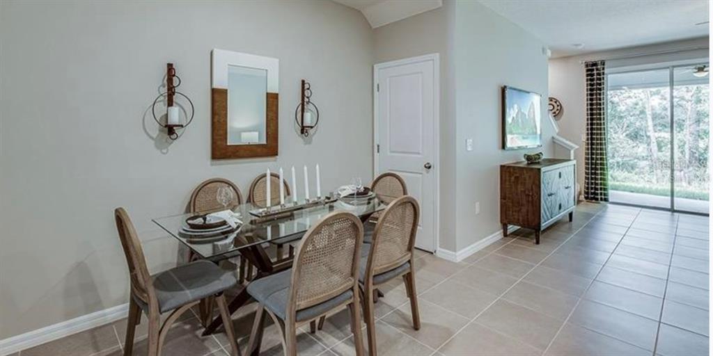 A dining room with a glass table, cane-back chairs, wall sconces, and a sliding door — 32971 PEZ LANDING LANE, WESLEY CHAPEL, FL