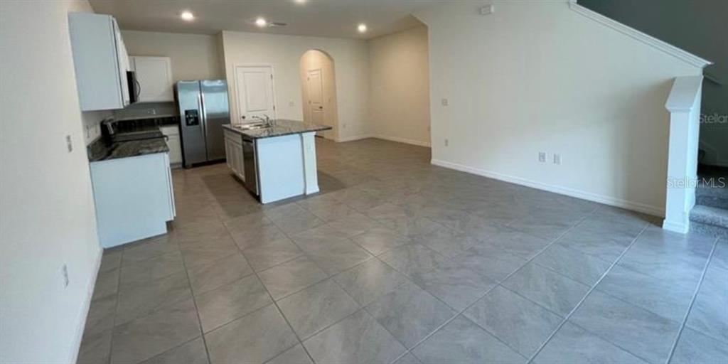 An open-concept kitchen features white cabinetry, granite countertops, stainless steel appliances, and gray tile flooring — 32971 PEZ LANDING LANE, WESLEY CHAPEL, FL
