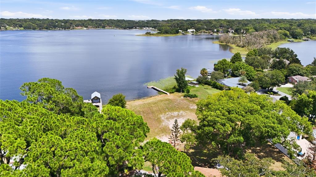 An aerial view shows a vacant waterfront lot with a dock on a large lake — 1810 PINEWAY COURT, MOUNT DORA, FL