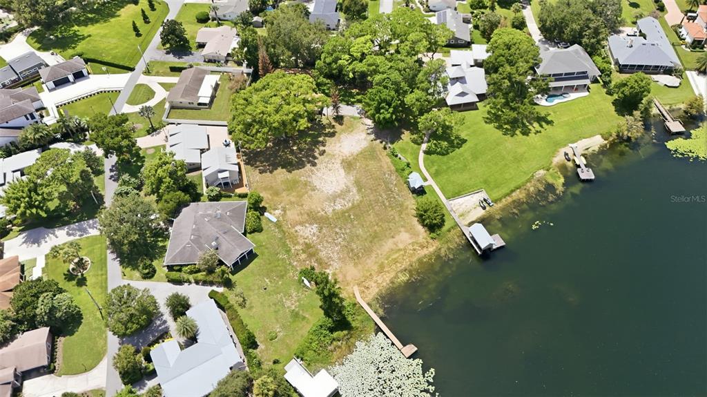 An aerial view shows a grassy waterfront lot with a boat dock at sunset — 1810 PINEWAY COURT, MOUNT DORA, FL
