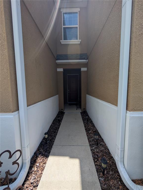 A concrete walkway leads to a recessed front door between two tan stucco walls — 17849 ALTHEA BLUE PLACE, LUTZ, FL