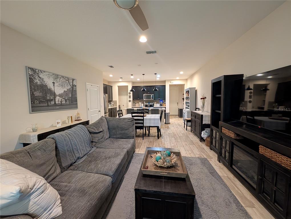 An open-concept living room and kitchen featuring gray tile flooring and dark wood furniture — 17849 ALTHEA BLUE PLACE, LUTZ, FL