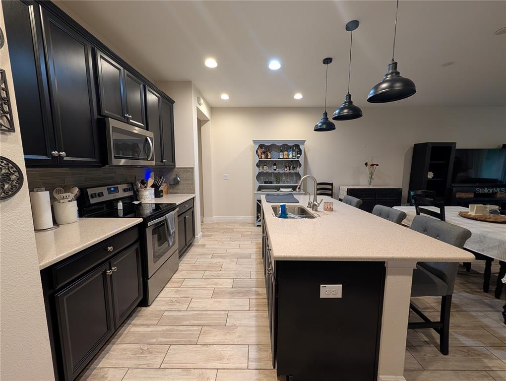 A kitchen features black cabinets, a large island with a sink, and light-colored tile flooring — 17849 ALTHEA BLUE PLACE, LUTZ, FL