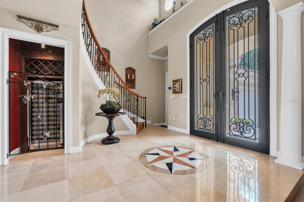 A grand foyer features a curved staircase, tile flooring with an inlay, and double iron doors — 2861 ROEHAMPTON CLOSE, TARPON SPRINGS, FL