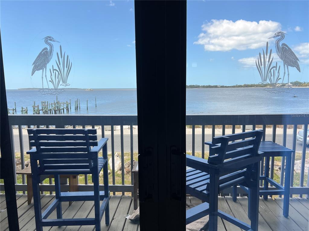 A view of a waterfront balcony with two blue chairs through glass sliding doors — 850 3RD STREET UNIT 2, CEDAR KEY, FL