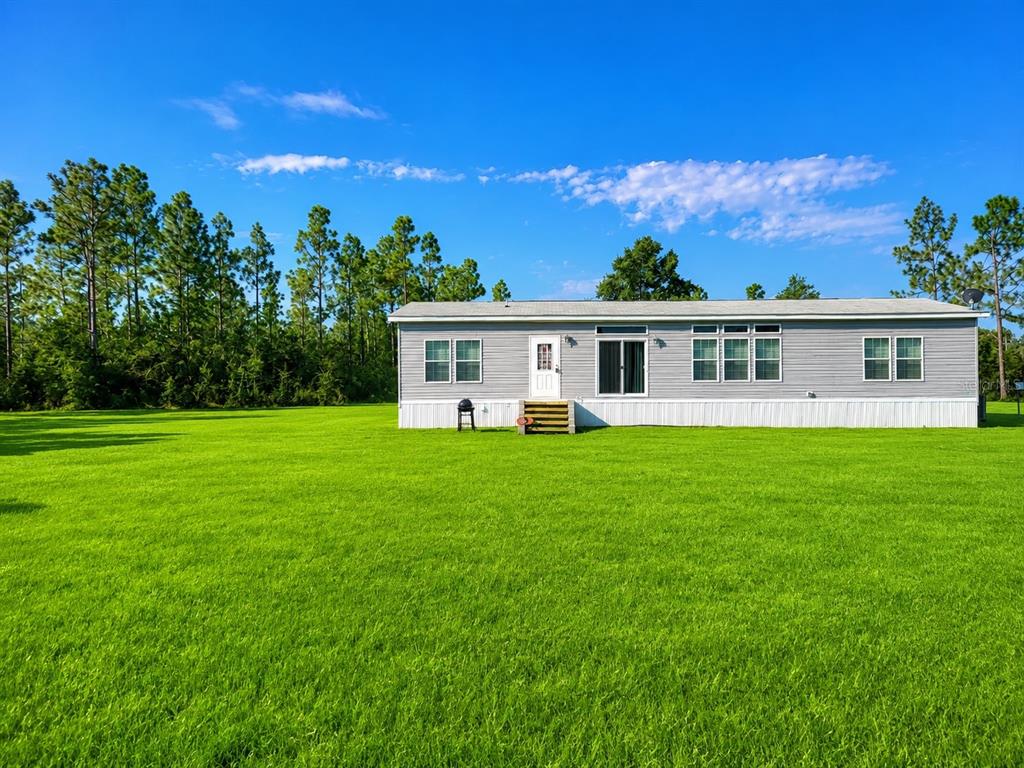 A single-story gray manufactured home sits on a large, flat green lawn near trees — 498 QUAIL HOLLOW BOULEVARD, CHIPLEY, FL