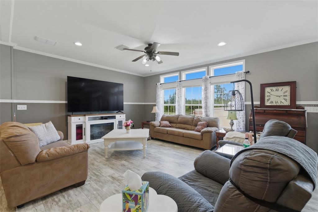 A living room features gray walls, wood-look tile flooring, a large television, and brown furniture — 498 QUAIL HOLLOW BOULEVARD, CHIPLEY, FL