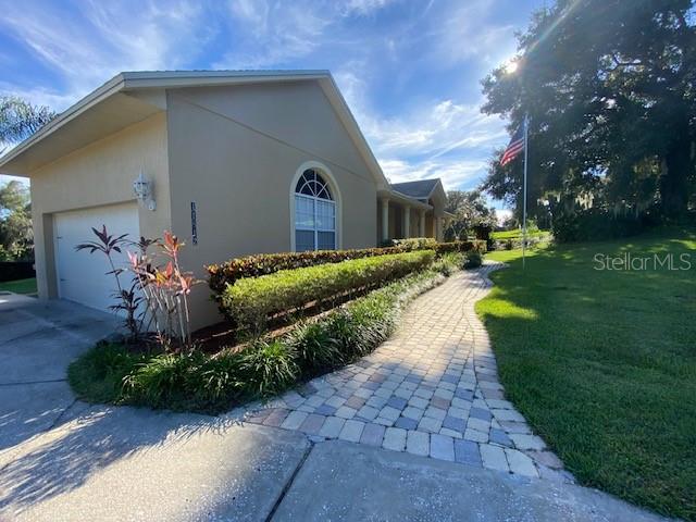 A paved walkway leads to the side entrance of a tan house with a garage — 11812 OSPREY POINTE BOULEVARD, CLERMONT, FL