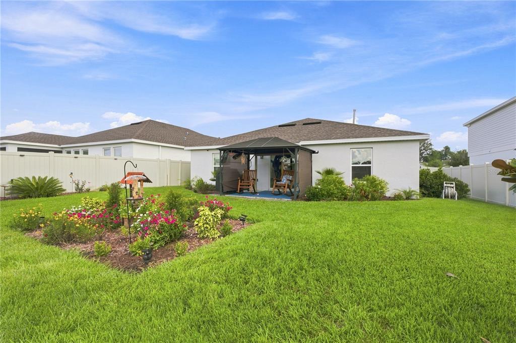 A backyard features a grassy lawn, a flower bed, and a covered patio area — 33647 SKY BLOSSOM CIRCLE, LEESBURG, FL