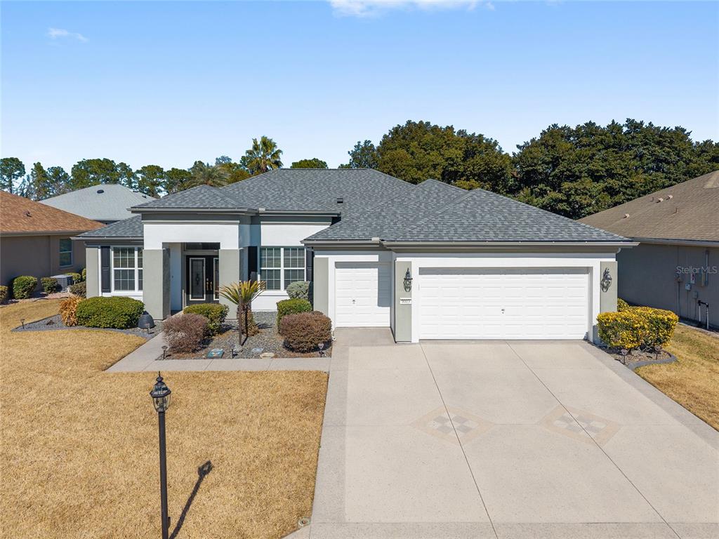 A single-story house with a gray shingled roof, white garage door, and landscaped front yard — 9003 SE 118TH LANE, SUMMERFIELD, FL