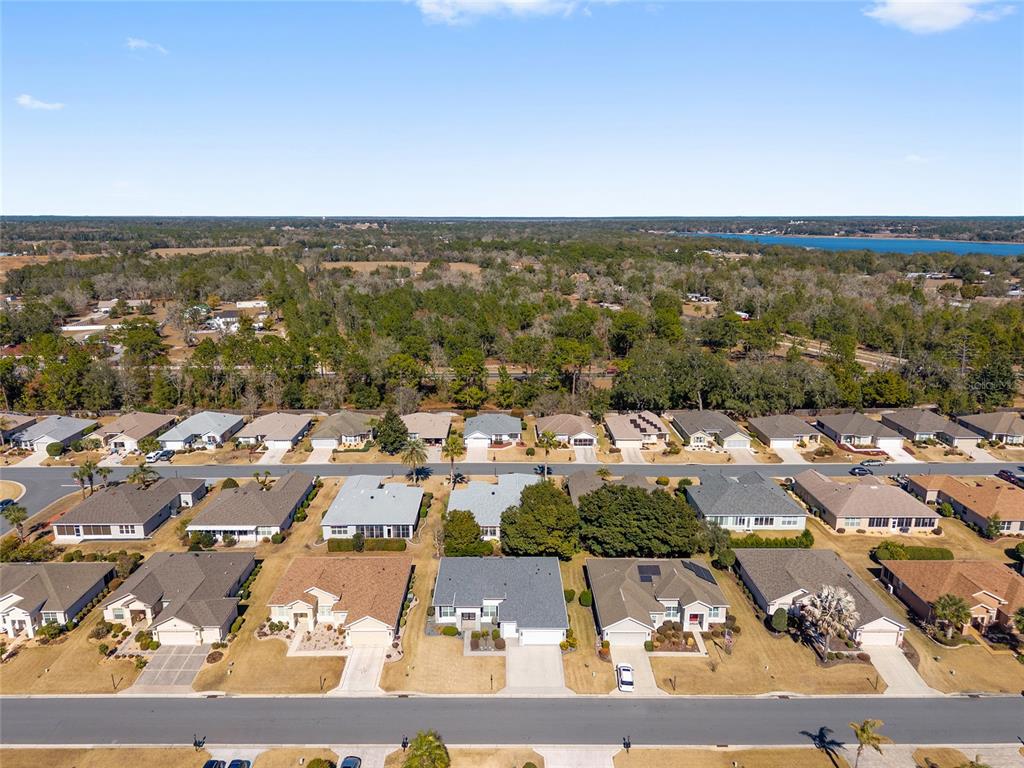 An aerial view shows a suburban neighborhood with single-family homes and a nearby lake — 9003 SE 118TH LANE, SUMMERFIELD, FL