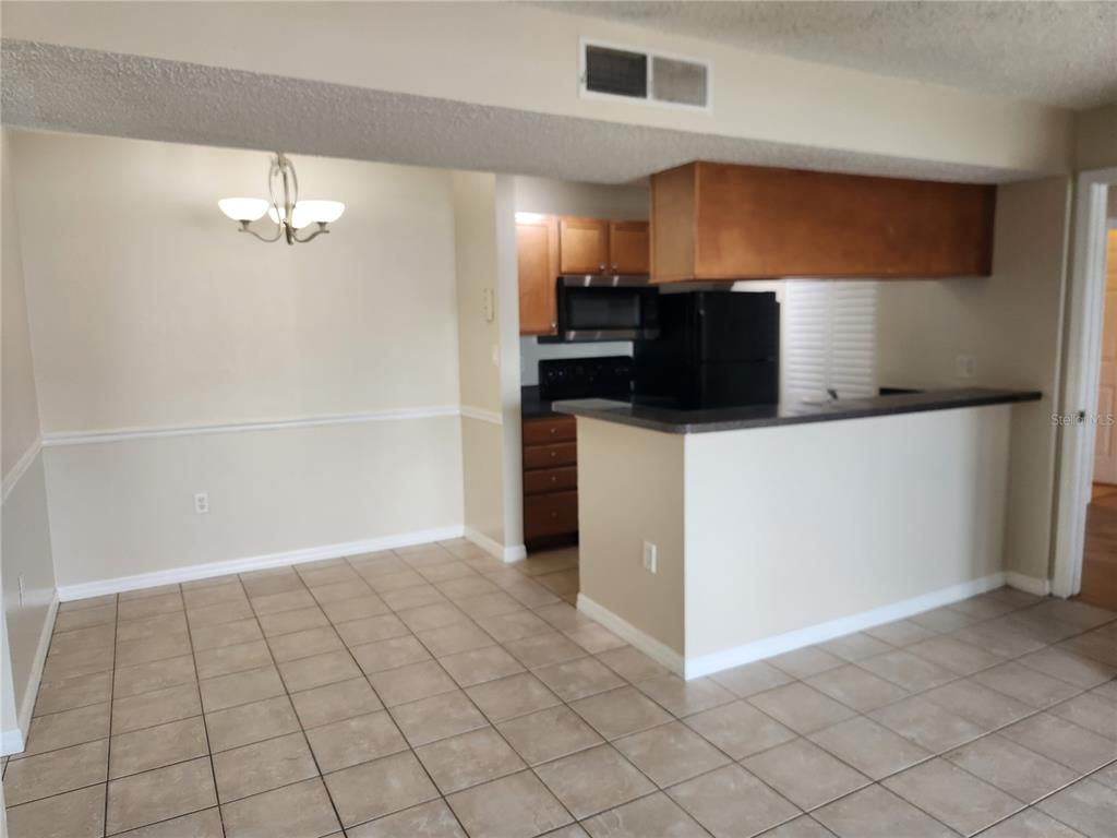 A dining area with tile floors leads to a kitchen featuring wood cabinets and a counter — 803 LAKE HAVEN SQUARE UNIT 101, BRANDON, FL