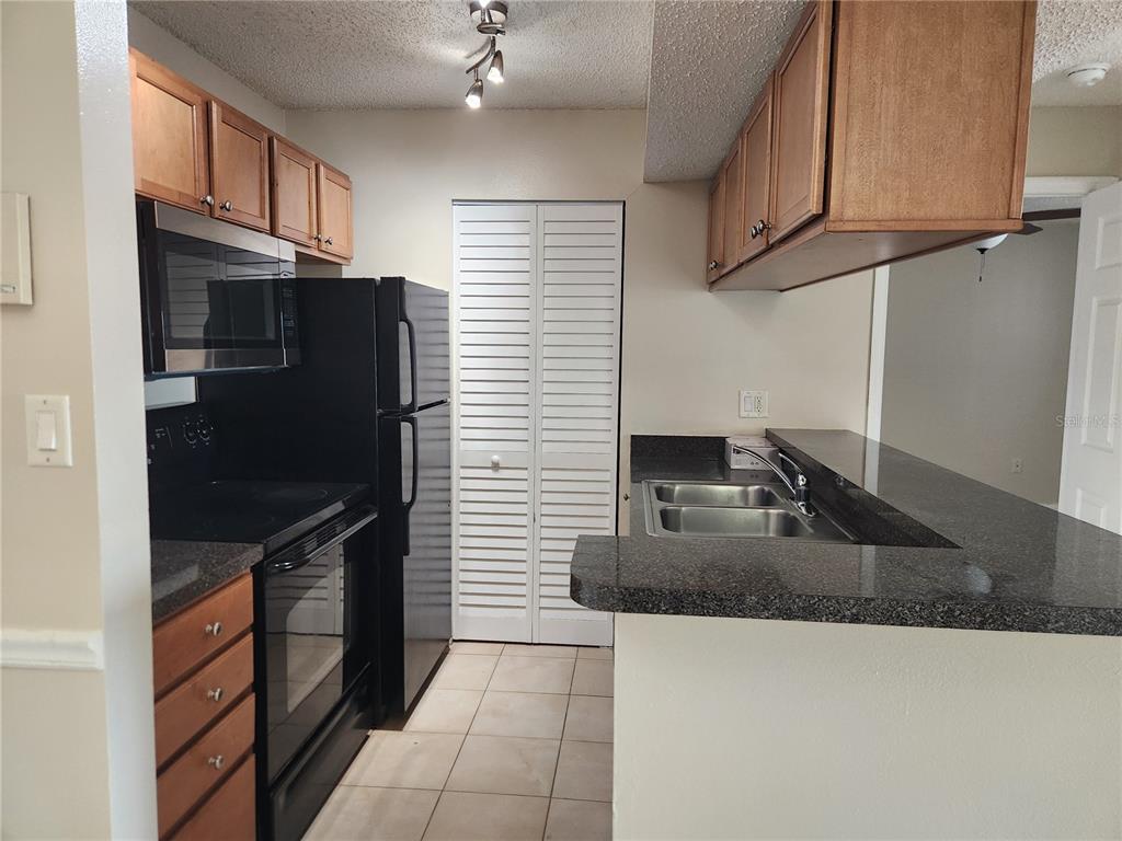 A kitchen features wood cabinets, black appliances, a dark countertop, and a tiled floor — 803 LAKE HAVEN SQUARE UNIT 101, BRANDON, FL