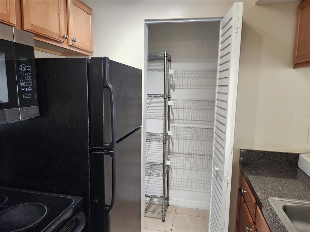 A kitchen features a black refrigerator, wooden cabinets, and a pantry with wire shelving — 803 LAKE HAVEN SQUARE UNIT 101, BRANDON, FL