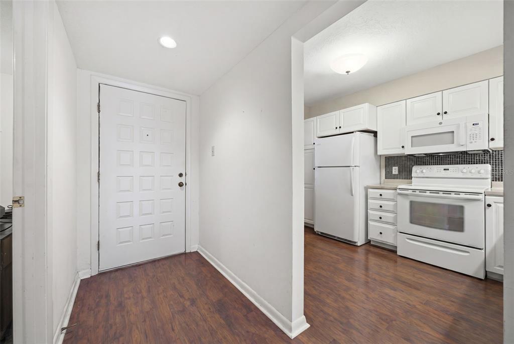 A white front door opens into a kitchen area with white appliances and wood flooring — 1802 MARINER DRIVE E UNIT 25, TARPON SPRINGS, FL