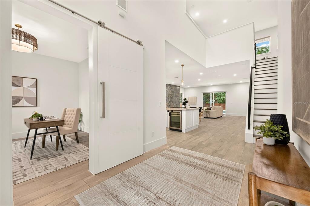 A bright entryway features a sliding barn door, wood-look flooring, and an open-concept living area — 2343 VERSAILLES AVENUE, WINTER PARK, FL