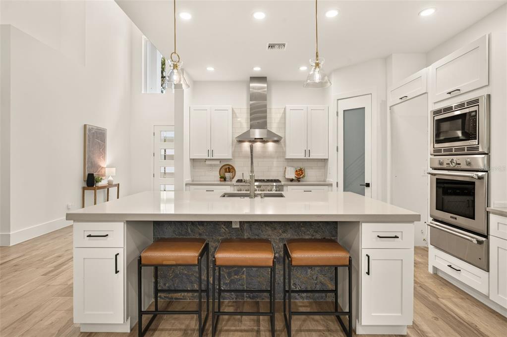 A modern kitchen features white cabinetry, a large quartz island with bar seating, and stainless appliances — 2343 VERSAILLES AVENUE, WINTER PARK, FL