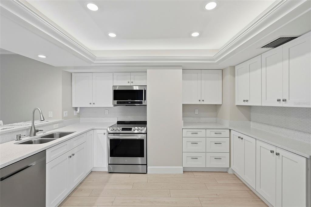 A modern kitchen features white cabinetry, stainless steel appliances, and a breakfast bar with stools — 1100 PINELLAS BAYWAY S UNIT G2, TIERRA VERDE, FL
