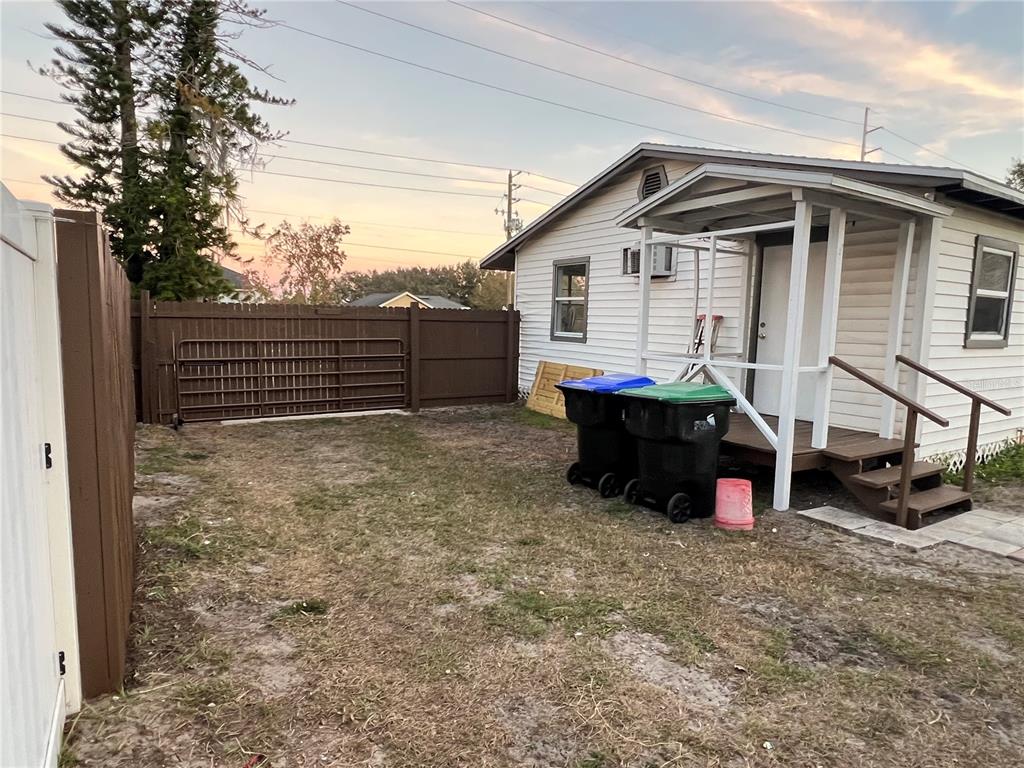 A small white house with a porch sits next to a fenced yard with trash bins — 1658 HEMPEL AVENUE, GOTHA, FL