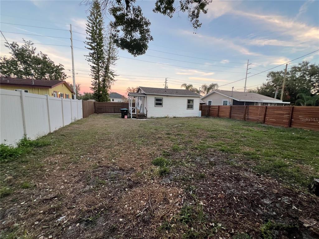 A backyard view showing a white house, a wooden fence, and a white vinyl fence — 1658 HEMPEL AVENUE, GOTHA, FL