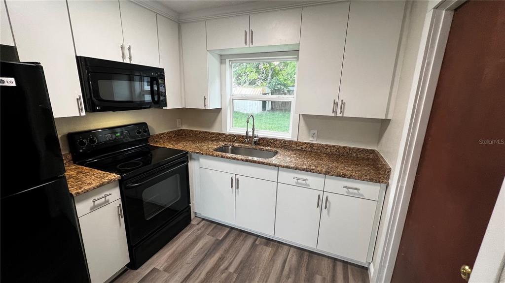 A kitchen features white cabinets, granite countertops, a black stove, and wood-look flooring — 1658 HEMPEL AVENUE, GOTHA, FL