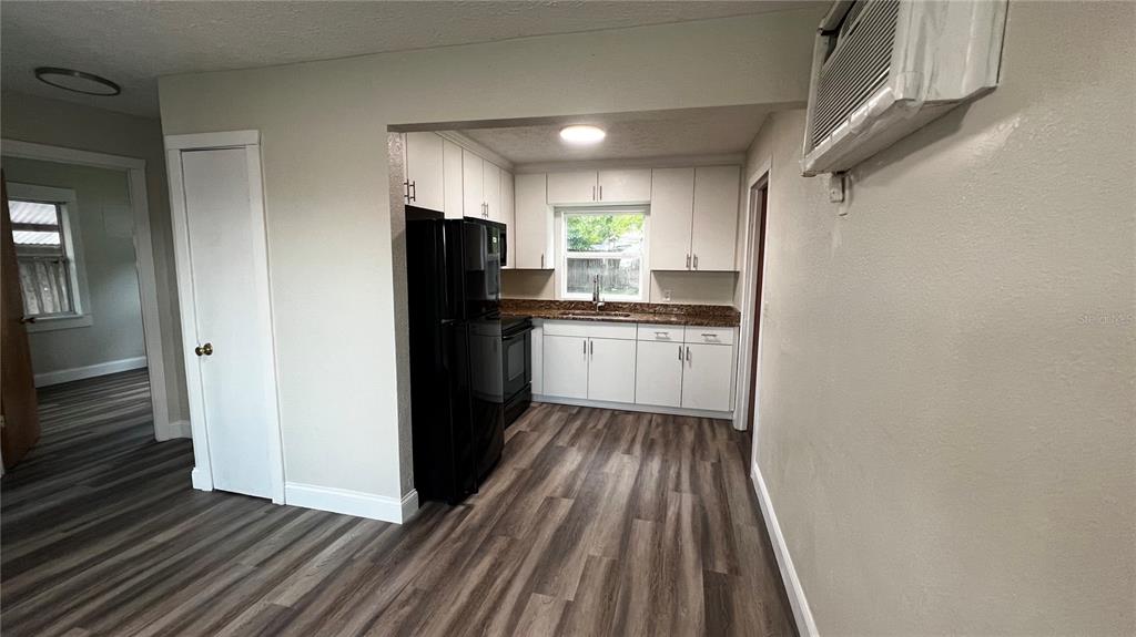 A kitchen features white cabinets, granite countertops, black appliances, and wood-look flooring — 1658 HEMPEL AVENUE, GOTHA, FL